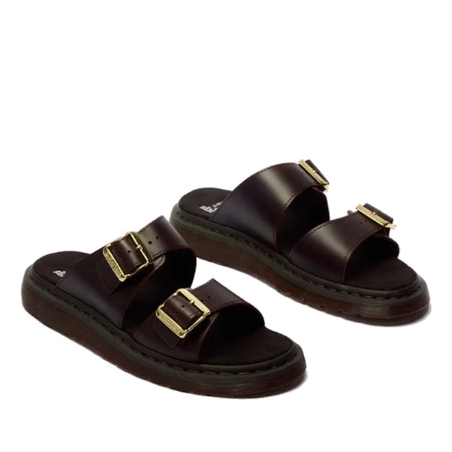 The Dr Martens Josef Charro Atlas Slide Sandal Leather features dark brown Atlas leather, two adjustable gold buckles per shoe, and thick textured brown soles.