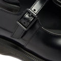 Close-up of Dr Martens Madaline Black Smooth Womens Slingback Mary Jane shoe with a shiny polished leather finish, featuring a strap and buckle detail, visible stitching, and part of the sole.