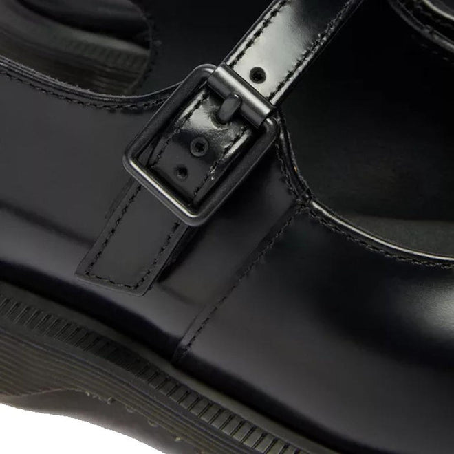 Close-up of Dr Martens Madaline Black Smooth Womens Slingback Mary Jane shoe with a shiny polished leather finish, featuring a strap and buckle detail, visible stitching, and part of the sole.