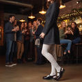 A woman in a dark dress, white lace tights, and Dr. Martens Madaline Cherry Red Arcadia Slingback Mary Jane Shoes stands in a bar, holding a small leopard-print purse as patrons laugh and chat by the counter.