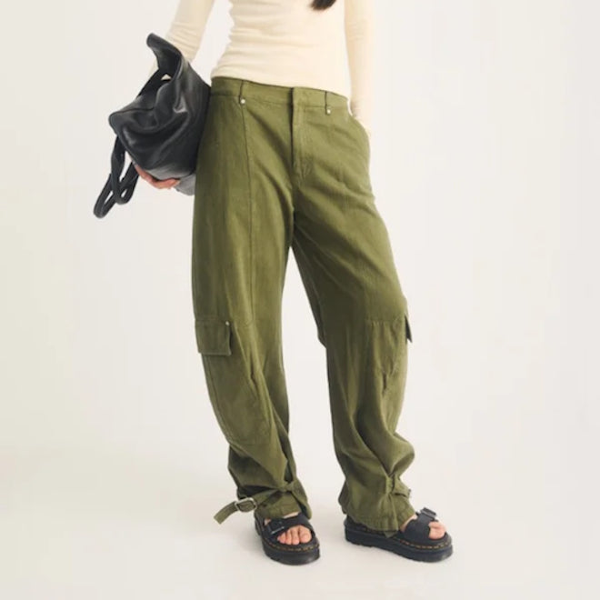 A person wearing olive green cargo pants and black Dr Martens Zebzag Black Pisa Leather 3 Strap Sandal, carrying a black handbag.