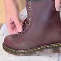 A person is lacing up a Dr Martens 1460 Cherry Red Crazy Horse Waxy Leather 8-eye Boot with yellow stitching on the Goodyear Welted sole, resting on white tissue paper with small black stars., 190665786835, 190665786842, 190665786859, 190665786873, 190665786880, 190665786897, 190665786910, 50000, 50001, 50002