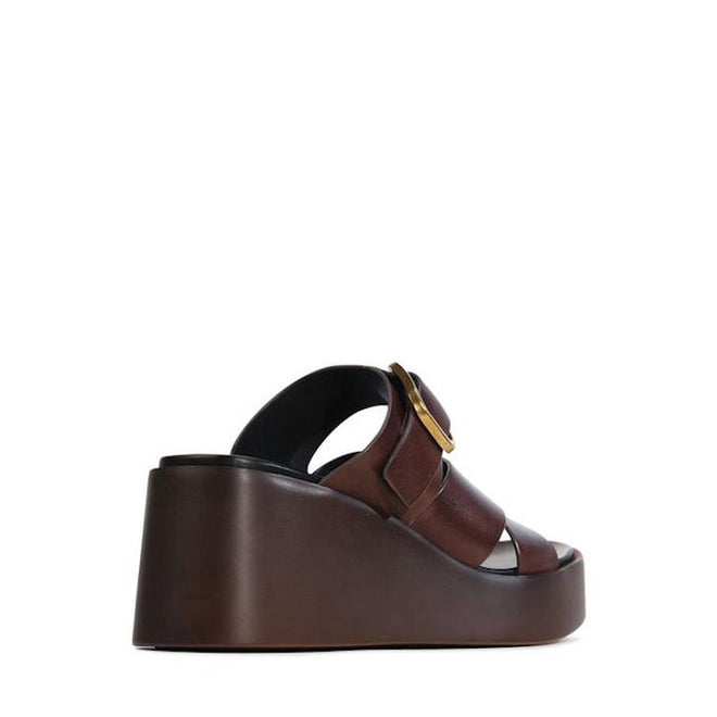 The EOS Aris Womens Chestnut Brown Leather Wedge Slide features an anatomical footbed, open toe, wide leather straps, and a large circular side buckle, shown in profile against a white background., 48005, 9321191293646, 9321191293653, 9321191293660, 9321191293677, 9321191293684, 9321191293691