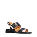 The EOS Ikam Womens Black Leather Low Heeled Sandal w/Back Strap features a wide front strap, open toe, low block heel, and an oversized gold buckle on the ankle strap. Shown in side profile against a white background.