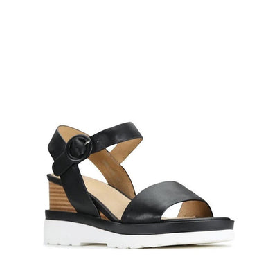 The EOS Jadon Black Leather Wedge Sandal features an open toe, thick white sole, brown stacked heel, and ankle strap with a large round buckle. Shown on a plain white background.