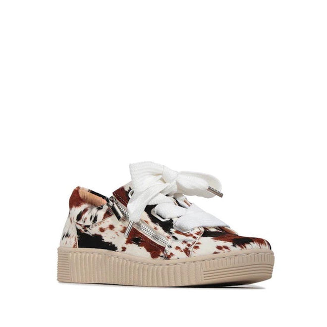 The EOS Jovi Texas Pony Leather Lace Up With Zip sneakers are low-top side zip shoes in a brown and white cow-print pattern, with thick white laces, silver side zippers, and a beige textured rubber sole, shown on a white background.