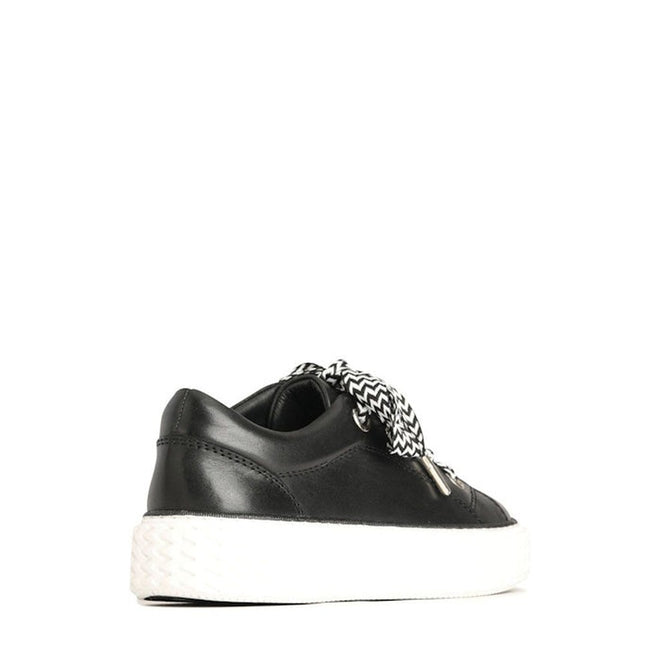 The EOS Trinsic Black Leather Lace Up Trainer is a black low-top sneaker in cashmere leather, shown from the rear side. It features black-and-white patterned laces, a chunky chevron outsole, and is set against a plain white background., 36520, 9321191200897, 9321191200903, 9321191200910, 9321191200927, 9321191200934, 36526
