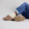 A person in rolled-up blue jeans, cream socks, and Emu Womens Eden Mushroom Platinum Sheepskin Scuff Slippers sits cross-legged on the floor, displaying the cozy slipper’s sole and top against a plain background., 9330071337912, 9330071337929, 9330071337936, 50731, 50732