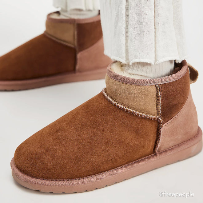 Close-up of a person wearing EMU Stinger Micro Patchwork Sheepskin Chestnut Wool Boots with white socks and light-colored pants. The chestnut boots feature soft sheepskin, water resistance, and a lighter brown panel at the back., 50669, 9330071977309, 9330071977316, 9330071977323, 50673, 50674