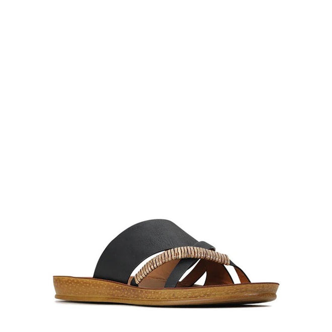 The Los Cabos Bride Black Flat Slide Sandal features a comfy, flat tan sole, wide black leather straps, and a decorative tan braided detail—perfect for resort wear. Photographed on a plain white background.
