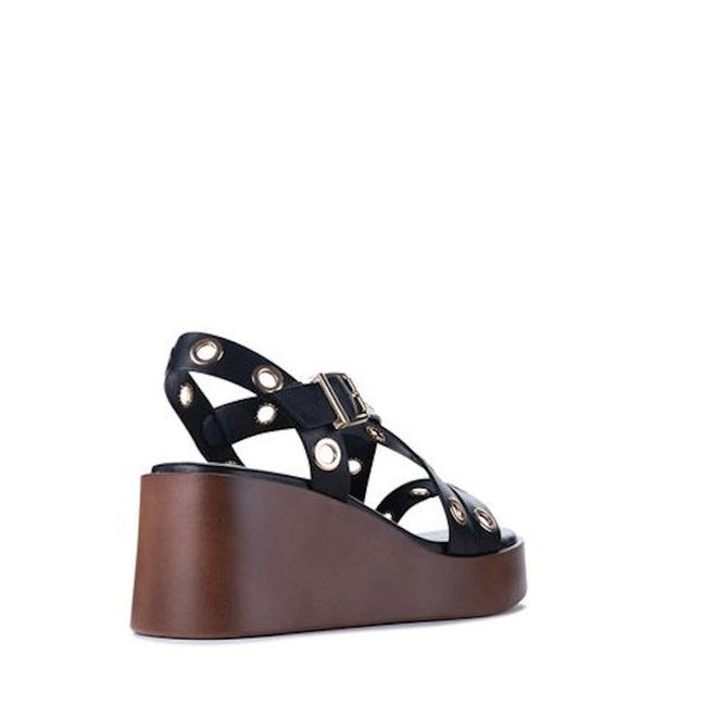 The Los Cabos Lagos Black Womens Wedge Heel Sandal, made from synthetic material, features ankle straps with metallic eyelets and a thick brown wedge heel. It's shown from the back-left side against a white background., 9321191309392, 9321191309408, 9321191309415, 9321191309422, 9321191309439, 46996
