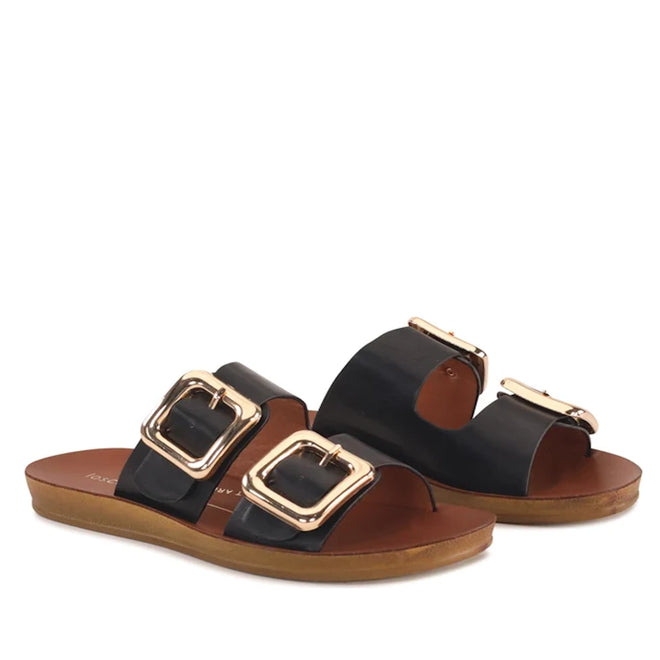 A pair of Los Cabos Womens Dina Black Light Flexible Two Strap Slide Sandals, featuring large gold buckles on brown anatomical footbeds with flat soles for comfortable arch support. The sandals are displayed at a slight angle against a white background.