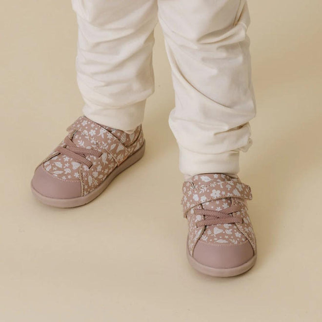 Child wearing pink Boston floral first walker sneakers with white pants on a beige background.,
9420075347922,
9420075347915,