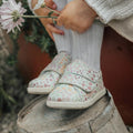 Children's floral shoes worn by a child sitting on a stone block with a blurred background.
9420075347700,