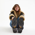 A smiling woman in a shearling jacket and jeans sits on the floor, legs extended to show the Vibram outsole of her Rollie Womens Chelsea Rise Vintage Mocha Leather Boots, against a plain white background., 9339554341682, 9339554341699, 9339554341705, 9339554341712, 9339554341729