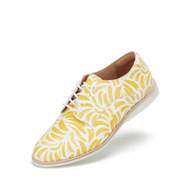The Rollie Womens Derby Sunshine Splash Leather Shoe features a premium leather upper with a yellow and white abstract leaf pattern, white sole, and lace-up design. Photographed against a plain white background.