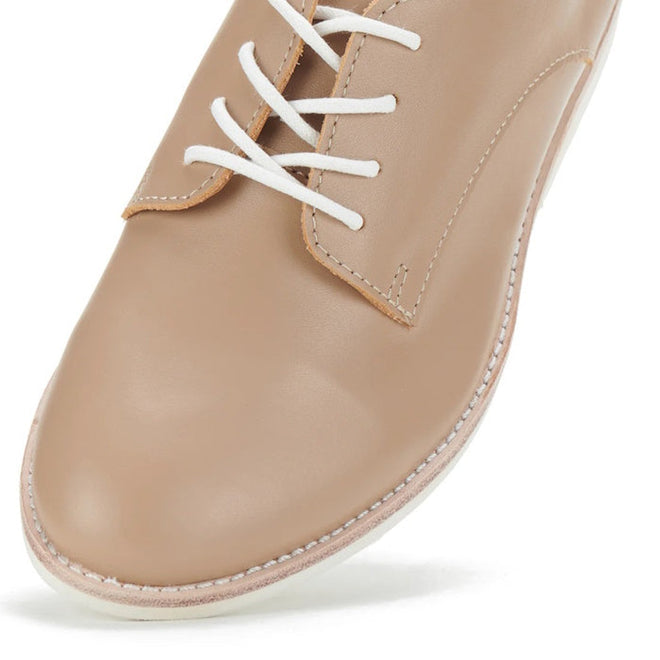 A close-up of the Rollie Womens Derby Super Soft Latte Leather Shoe, featuring beige premium leather, white laces, white sole stitching, and a sleek minimalist design that emphasizes sneaker-like comfort and a stylish silhouette., 9781760763848, 9781760763855, 9781760763862, 9781760763879, 9781760763886