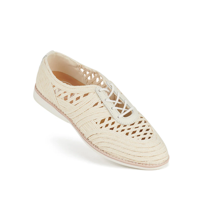 The Rollie Womens Derby Open Weave Oat Off White Trainer is a cream-colored woven lace-up oxford with cutout details, a removable footbed, rounded toe, and flat sole, displayed at an angle on a white background.