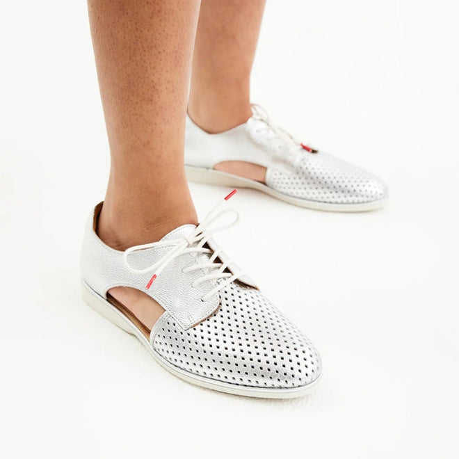 A person wears the Rollie Womens Sidecut Punch Silver Metallic Leather Shoe on a white surface. This breathable shoe features cut-out sides, white laces, a low heel, and an anti-slip rubber outsole for comfort and stability., 9339554231341, 9339554231358, 9339554231365, 9339554231372, 9339554231389