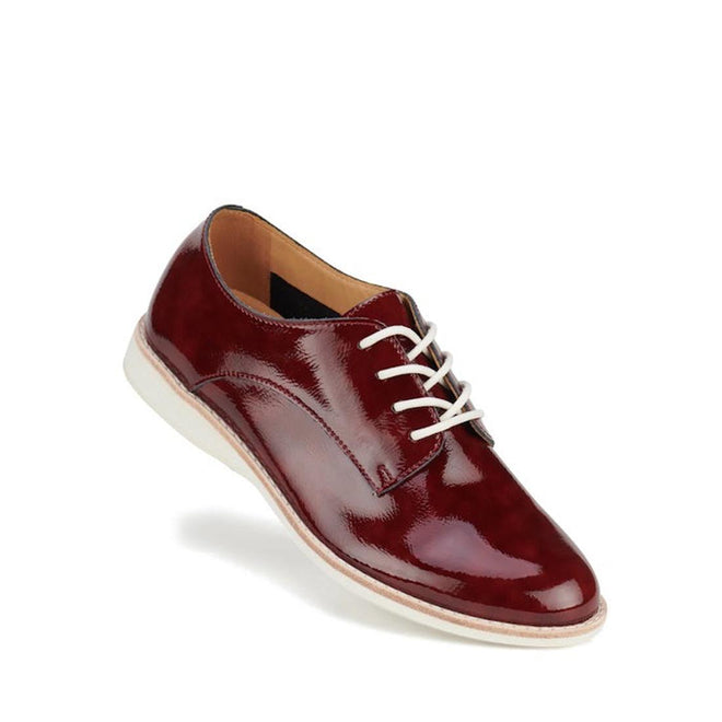Right foot showing the front and outer side of a shiny burgundy Rollie Derby crinkle patent brogue shoe with white laces on a white background