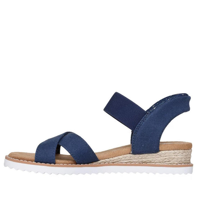 The Skechers Womens Bobs Desert Kiss Golden Lily Navy SLIP IN is a blue open-toe sandal with crisscross fabric and ankle straps, a tan Memory Foam footbed, woven espadrille-style midsole, and white ridged outsole, shown in side profile., 49030, 198739558746, 198739558760, 198739558784, 49034, 49035