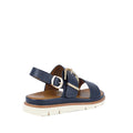The Soultbush Garie Navy Blue Womens Sandal with Back Strap features a cushioned footbed, tan sole, gold buckle, and crisscross straps. Shown from the side and slightly behind on a white background, this sandal is perfect for effortless coastal living.
