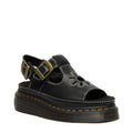 The Dr Martens Dunnet Flower Sandal Black Quad Platform features a black full-grain leather upper with floral cutouts, peep toe, white stitching, adjustable ankle strap with gold buckle, and a thick black sole accented by yellow stitching.