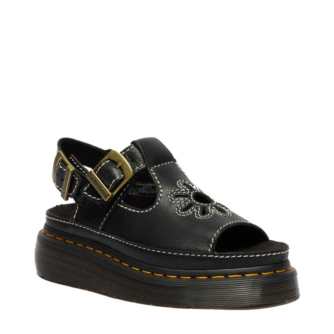 The Dr Martens Dunnet Flower Sandal Black Quad Platform features a black full-grain leather upper with floral cutouts, peep toe, white stitching, adjustable ankle strap with gold buckle, and a thick black sole accented by yellow stitching.