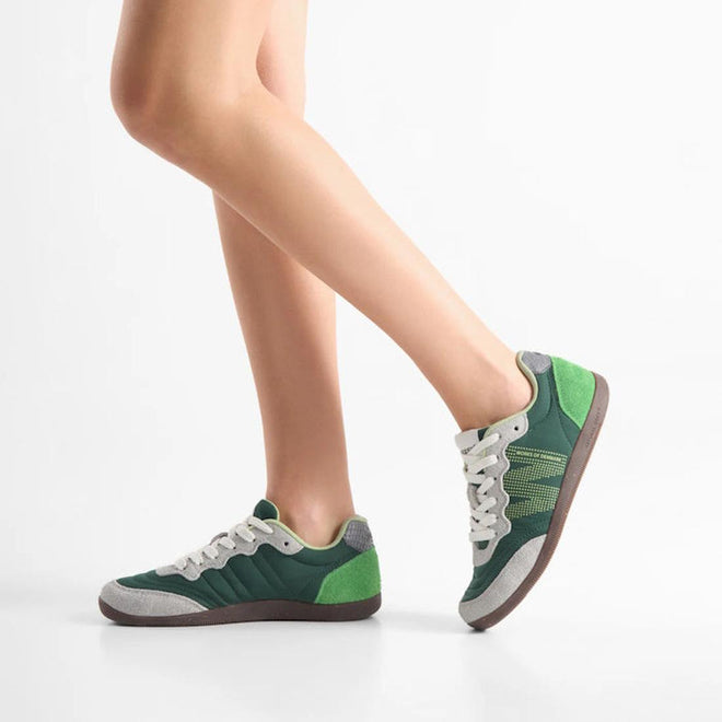A person wears Woden Nanna Apple Green Multi Lace Up Sneakers, featuring green and gray accents with white laces, standing on one leg with the other bent slightly in front against a plain white background., 50250, 5713326697834, 5713326697841, 5713326697858, 50253