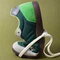 The Woden Nanna Apple Green Multi Lace Up Sneaker, featuring a brown sole and white laces, is flexed heel to toe against an olive-green background, showcasing its packable, travel-friendly design., 50250, 5713326697834, 5713326697841, 5713326697858, 50253
