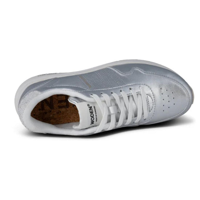 The Woden Womens Sneaker Nora Natural Soft Metallic Silver, shown from above at an angle, features silver and white tones, white laces, a cork insole, perforated toe, visible WODEN branding on the tongue, and upcycled fish leather for sustainability., 42438, 5713326588613, 5713326588620, 5713326588637, 5713326588644, 42443