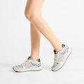 A person wearing Woden Rigmor Animal Damlation Lace Up Sneakers in light gray and white with black accents, made from LWG certified leather, stands on a white background. Only the lower legs and feet are visible., 5713326695267, 5713326695274, 5713326695281, 5713326695298, 5713326695304, 5713326695311