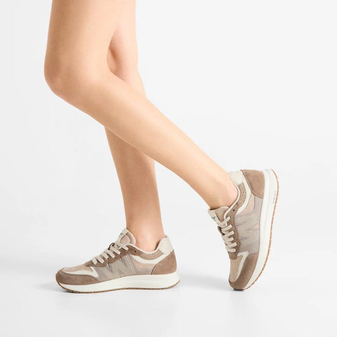 A person with bare legs wears Woden Rigmor Heritage Coffee Cream Lace Up Sneakers featuring beige laces and LWG certified suede, standing on one leg with the other slightly bent against a plain white background., 50259, 5713326695113, 5713326695120, 5713326695137, 50263, 50264