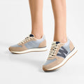 A person stands on a white background, showing only their lower legs and feet in Woden Ronja Icon Moonstone Multi Lace Up Sneakers featuring light blue, beige, and gray colors with recycled mesh panels, white laces, and gum soles., 50270, 5713326699678, 5713326699685, 5713326699692, 50274