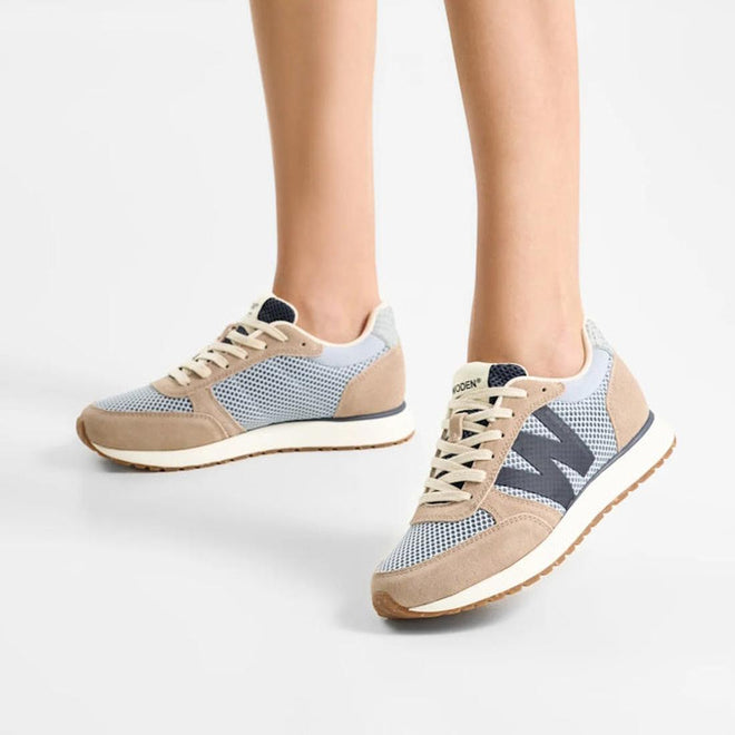 A person stands on a white background, showing only their lower legs and feet in Woden Ronja Icon Moonstone Multi Lace Up Sneakers featuring light blue, beige, and gray colors with recycled mesh panels, white laces, and gum soles., 50270, 5713326699678, 5713326699685, 5713326699692, 50274