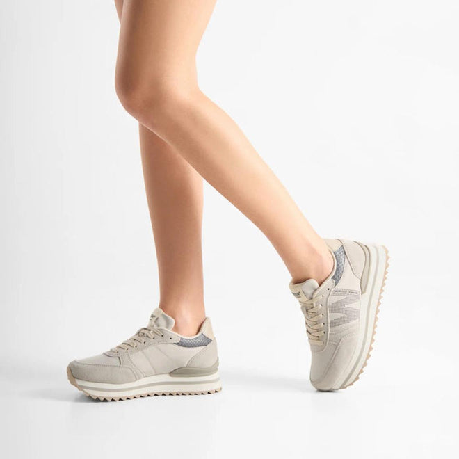 A person balances on one leg with the other bent, showcasing Woden Ronja Plateau Delpin Lace Up Sneakers made from sustainable materials. Only the legs and sneakers appear against a plain white background., 5713326692365, 5713326692372, 5713326692389, 5713326692396, 5713326692402
