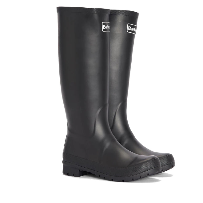 The Barbour Abbey Black Tall Welly Women's Rainboot features textured soles and a front Barbour logo. These classic black rubber rain boots stand upright on a white background, offering a timeless high welly style.