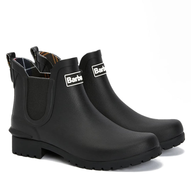 The Barbour Wilton Black Chelsea Wellingtons Womens Rainboot features elastic sides, pull tabs, rugged soles, and a tartan lining, shown against a white background.
