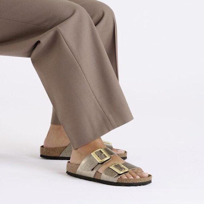 Person wearing brown sandals with gold buckles and beige pants on a light gray background,
4066648998228,
4066648998266,
4066648998303,