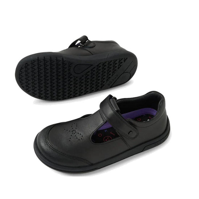 The Bobux Kid+ Black School Leather Shoe Bubbles T Bar is a children's black premium leather T-bar shoe with a round toe, perforated front, hook-and-loop strap, and scuff-resistant sole—shown side-on and with its tread pattern visible.