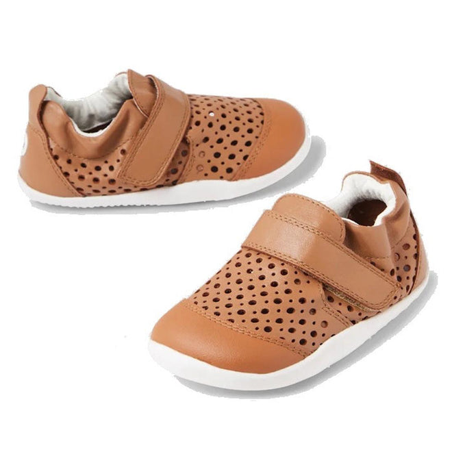 A pair of Bobux Punch first walking crawing shoes with holes over the top of the foot for breathability and a single velcro strap over the top of the foot.Eleastic at the heel and reenforced toe brown children's shoes with white soles on a white background.,