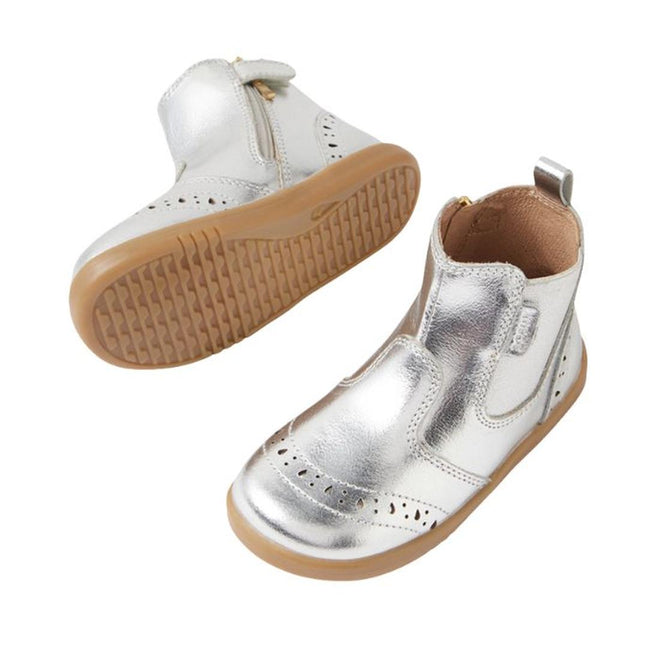 The Bobux IW Iwalk Billie Jodhpur Girls Leather Boot in silver features shiny leather, light brown flexible soles, a side zipper, and decorative perforations. One boot stands upright while the other shows its sole., 9420074856302, 9420074856319, 9420074856326, 9420074856333, 9420074856340