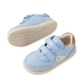 A pair of Bobux IW Iwalk Toddlers Champ Leather Sneakers in Skyway Blue, featuring light blue leather uppers, white soles, hook-and-loop straps, and a tan heel accent. One sneaker stands upright while the other lies on its side to showcase the tread pattern of the sole., 9420074856753, 9420074856760, 9420074856777, 9420074856784, 9420074856791