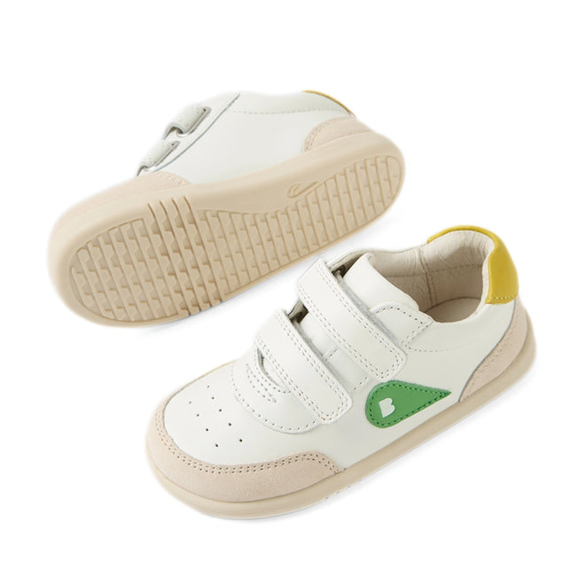 Two Bobux IW Iwalk Toddlers Champ Leather Sneakers in white leather, featuring beige soles, green and yellow accents, and double hook-and-loop straps. One sneaker is upright showing the top view, while the other is flipped to reveal the sole., 9420074856609, 9420074856616, 9420074856623, 9420074856630, 9420074856647