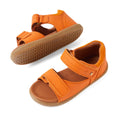 Two Bobux IWalk Driftwood Sandal Orange Peel open-toe leather sandals for toddler boys are displayed: one upright and the other on its side to showcase the light brown, textured rubber sole. These sandals feature adjustable Velcro straps and are designed to offer comfort and breathability, making them ideal for active little ones., 9420074807656, 9420074807663, 9420074807670, 9420074807687, 9420074807694