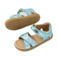 Two Bobux IWalk Flora Toddlers Sandal Jelly Mint Metallic Blue Open Toe sandals for children feature light blue straps, pastel star and rainbow patterns, tan footbeds, and rubber outsoles. One sandal is upright while the other is flipped to display the sole—charming metallic blue sandals perfect for any little one’s adventures.