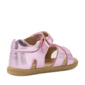 Introducing the Bobux IWalk Flora Toddlers Sandal in Pink Lemonade: a stylish metallic pink sandal for toddlers featuring a closed heel, velcro strap, and open toe design. Crafted from breathable leather, this toddlers’ leather sandal is finished with a light brown sole embossed with “BOBUX” on the side. The product is displayed against a white background.