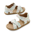 Two pairs of Bobux IWalk Flora Toddlers Sandal White Floral Open Toe are displayed, each featuring light-colored soles and white leather straps with a delicate floral pattern and adjustable Velcro closures. Crafted for all-day comfort, one sandal lies flat while the other is slightly tilted to showcase its high-quality design.