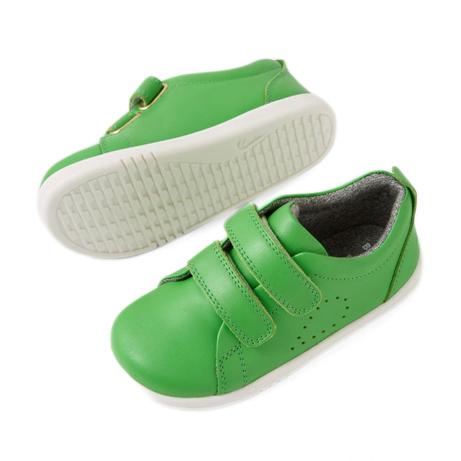 A pair of Bobux Iwalk Toddlers Grass Court Retro Green Leather Trainers, featuring white soles, Velcro straps, and small ventilation holes on the side. One shoe is lying flat while the other is on its side showcasing the sole—perfect toddler trainers for everyday adventures., 9420074806789, 9420074806796, 9420074806802, 9420074806819, 9420074806826