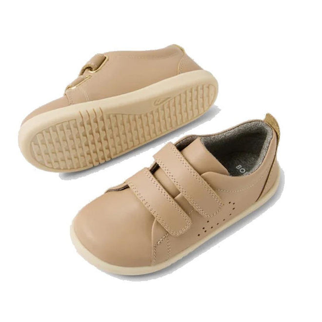 The Bobux IW Iwalk Grass Court Leather Sneaker in Warm Taupe features a premium leather upper, rounded toes, rubber soles, and two Velcro straps. One shoe is shown upright from the top and side; the other highlights the textured sole., 9420074803368, 9420074803375, 9420074803382, 9420074803399, 9420074803405